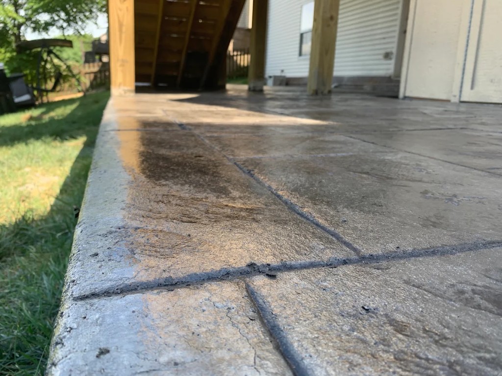 Stamped concrete patio with tooled control joints poured under a backyard deck