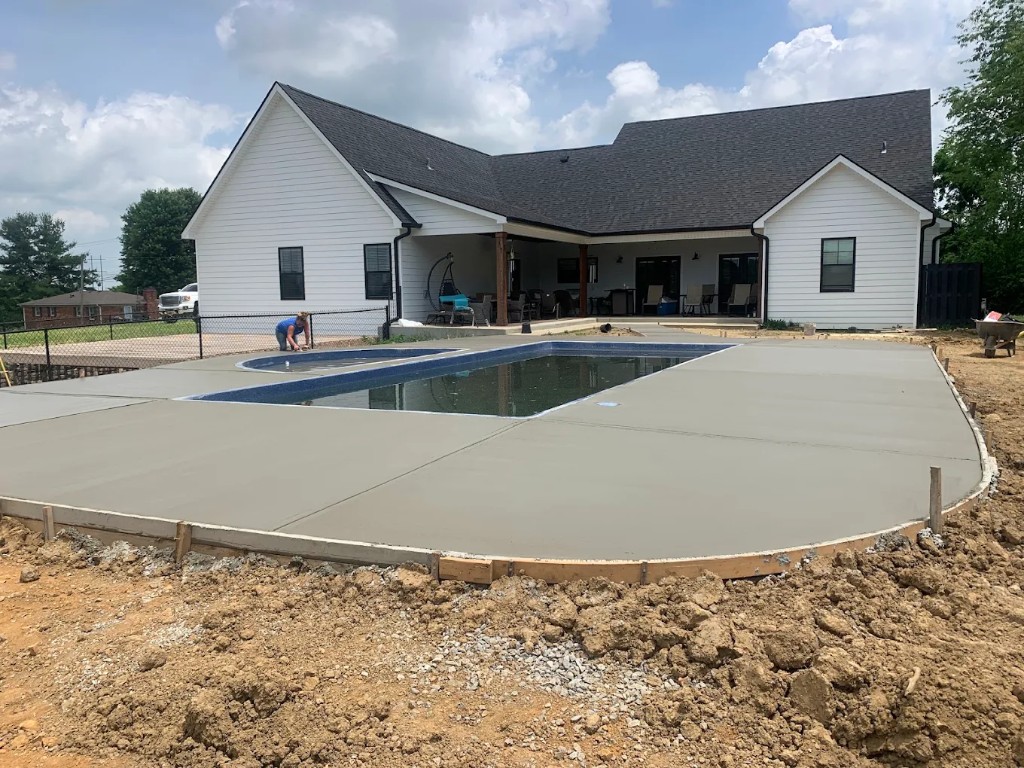 Large concrete pool deck in front of a white farmhouse