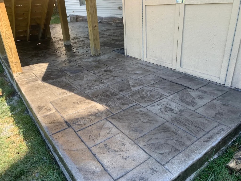 Stamped concrete pad between porch posts and a garage